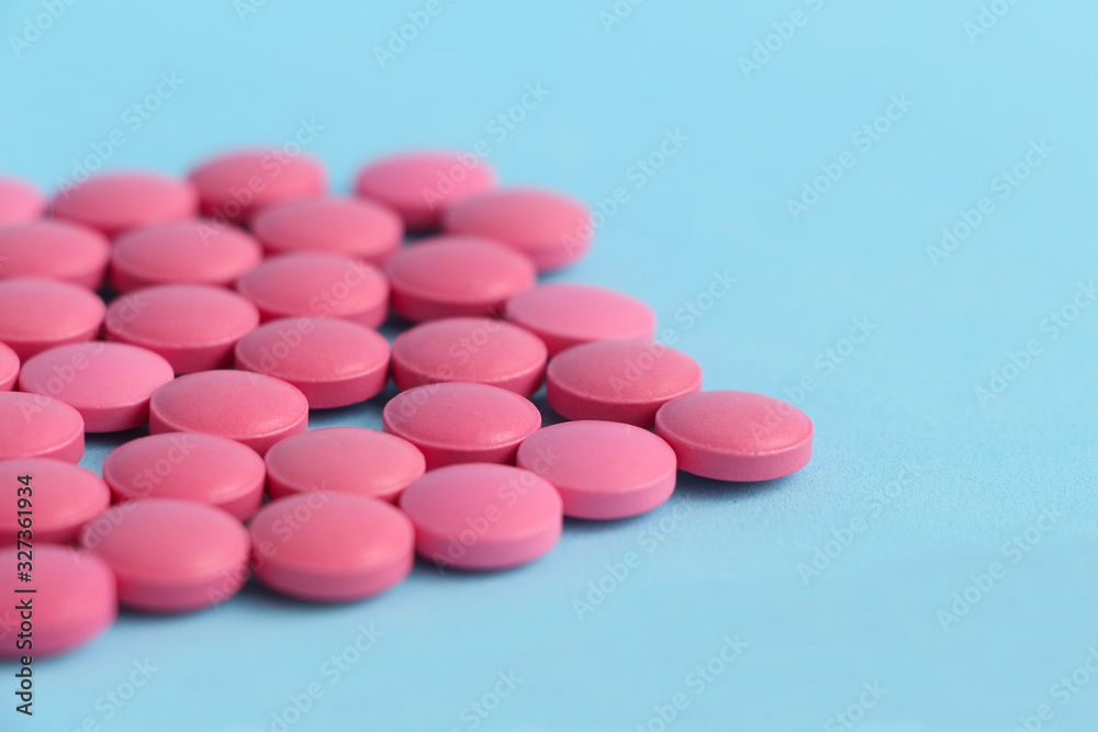 Group of pink round pills on a blue background. Selective focus. Theme of health care, medical treatment and disease prevention. Group of pink round pills on a blue background. Selective focus. Theme of health care, medical treatment and disease prevention.