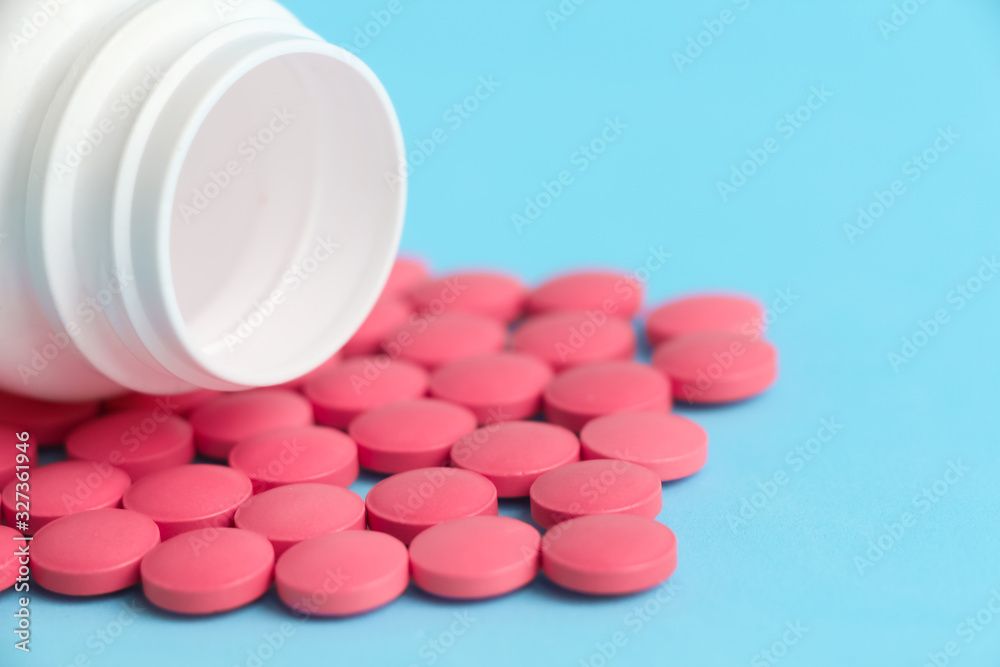Group of pink round medicine pills and white bottle on a blue background. Selective focus. Theme of health care, medical treatment and disease prevention. Group of pink round medicine pills and white bottle on a blue background. Selective focus. Theme of health care, medical treatment and disease prevention.