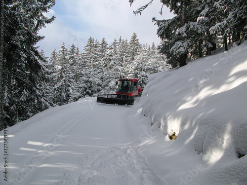 Winter landscape, snowy forest and road. Tractor cleans a road in the mountains, Austrian Tyrol