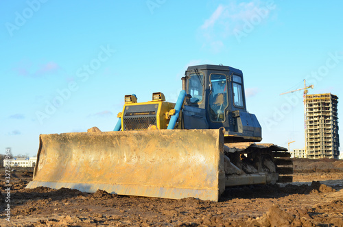Bulldozer during land clearing and foundation digging at large construction site.  Crawler tractor with bucket for pool excavation and utility trenching. Dozer  Earth-moving equipment.