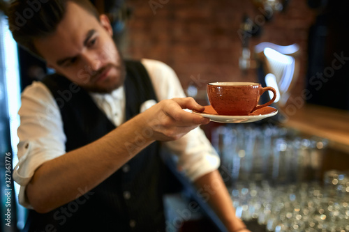 handsome waiter looking at the orange cup and soucer before giving them to a client. close up photo. blurred background