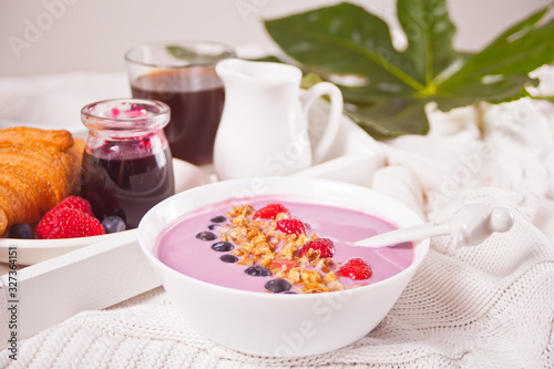 Smoothie bowl with berries. Croissant bun, glass of coffee, jar of milk, jam nearby.
