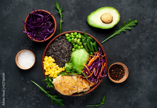 Bowl Buddha.Quinoa, chicken breast, avocado, red cabbage, arugula, carrot, green peas, corn, broccoli, green beans in a plate on a stone background.