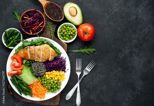 Bowl Buddha.Quinoa, chicken breast, arugula, avocado, red cabbage, carrot, green peas, corn, tomato, green beans in a white plate on a stone background. with copy space for your text