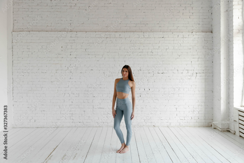 Attractive young brunette fitness woman in top and leggings against a white brick wall. Studio shot. Attractive young brunette fitness woman in top and leggings against a white brick wall. Studio shot.