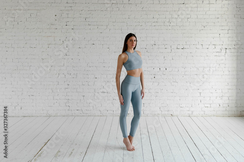 A girl in a sports top and leggings stands against a white brick wall photo
