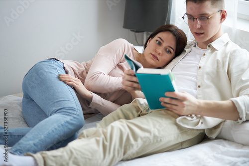 A young handsome clever man is reading a book to his wife ,close up side view photo, education, bookworms. free time, spare time, lifestyle
