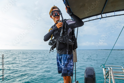 young diver in a suit and diving equipment is preparing to jump from boat into the water