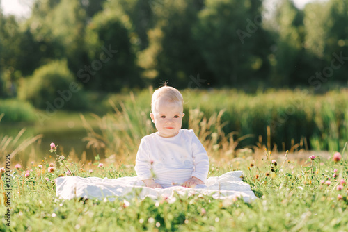 A small child sits on a blanket on the shore of the lake in the open air. Summer walks with your baby