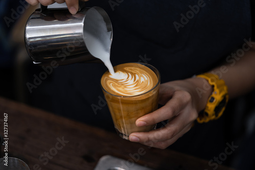 Close-up of barista hand holding and pouring hot milk for prepare latte art on piccolo latte cup of coffee. photo