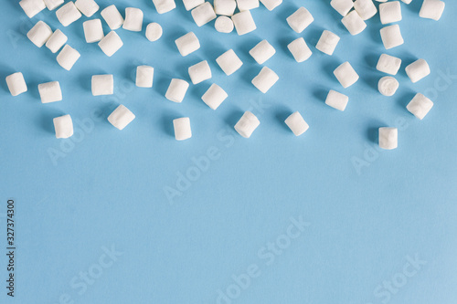 Frame of white marshmallows on a blue background. Flatlay or top view. Background of white mini marshmallows. Concept of snow, winter mood, food.