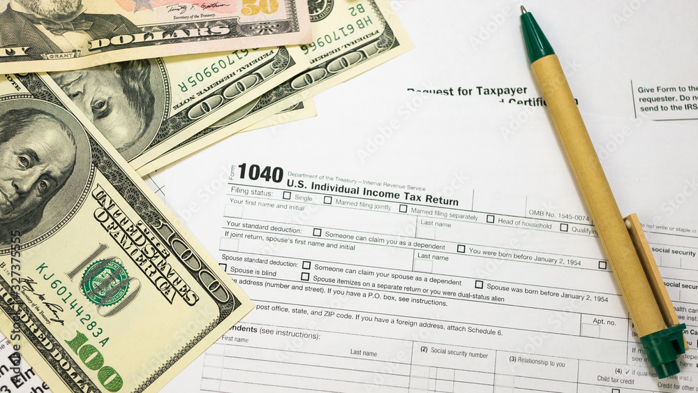 IRS 1040 U.S. Tax Form and U.S. Dollar Banknotes with Green Pen. Wage and tax statement concept. IRS 1040 U.S. Tax Form and U.S. Dollar Banknotes with Green Pen. Wage and tax statement concept.