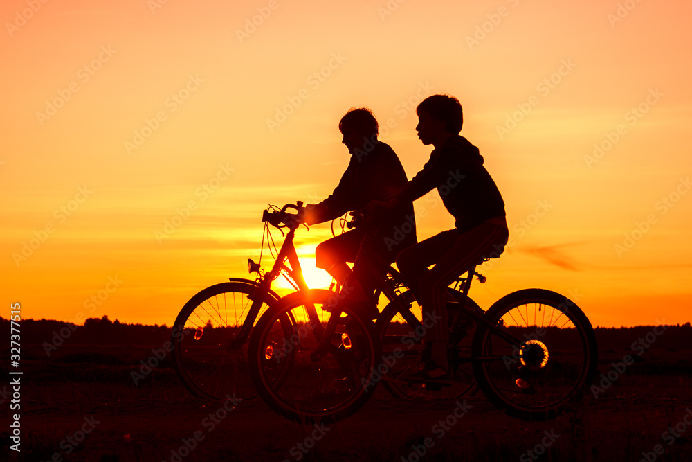 Obraz premium Boy and senior woman riding bikes, silhouettes of riding persons at sunset in nature