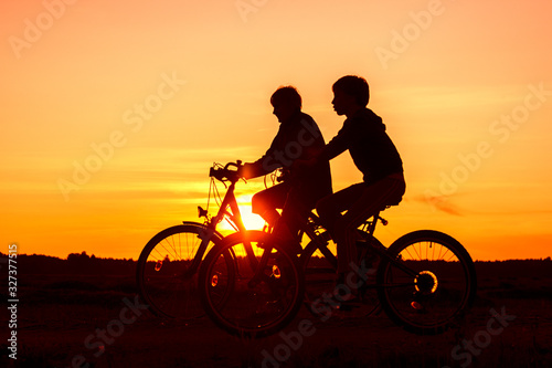 Boy and senior woman riding bikes, silhouettes of riding persons at sunset in nature