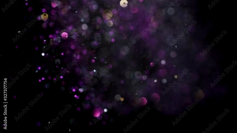 Gold and silver and purple glitter flying after being exploded, bright particles bouncing against camera flying and falling down on black background. Top view close up macro slow motion
