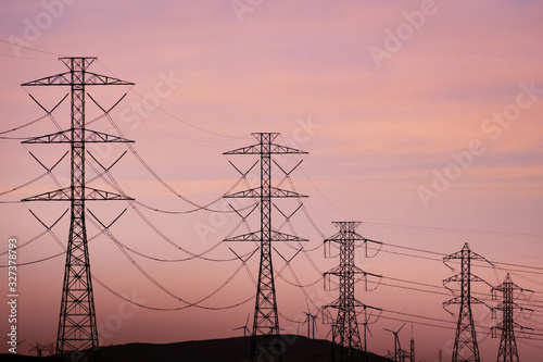 Sunset view of high voltage electricity towers on the hills of San Francisco bay area; Wind turbines visible in the background; California