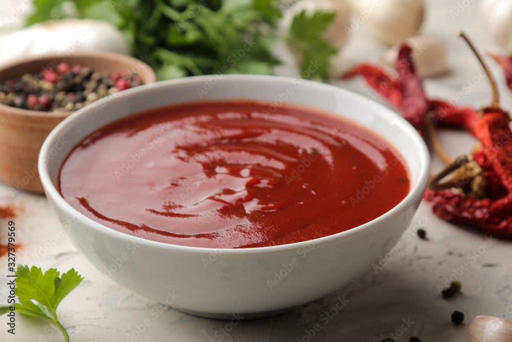 Red sauce or ketchup in a bowl and ingredients for cooking, spices, garlic, pepper and herbs on a light concrete background. Red sauce or ketchup in a bowl and ingredients for cooking, spices, garlic, pepper and herbs on a light concrete background.