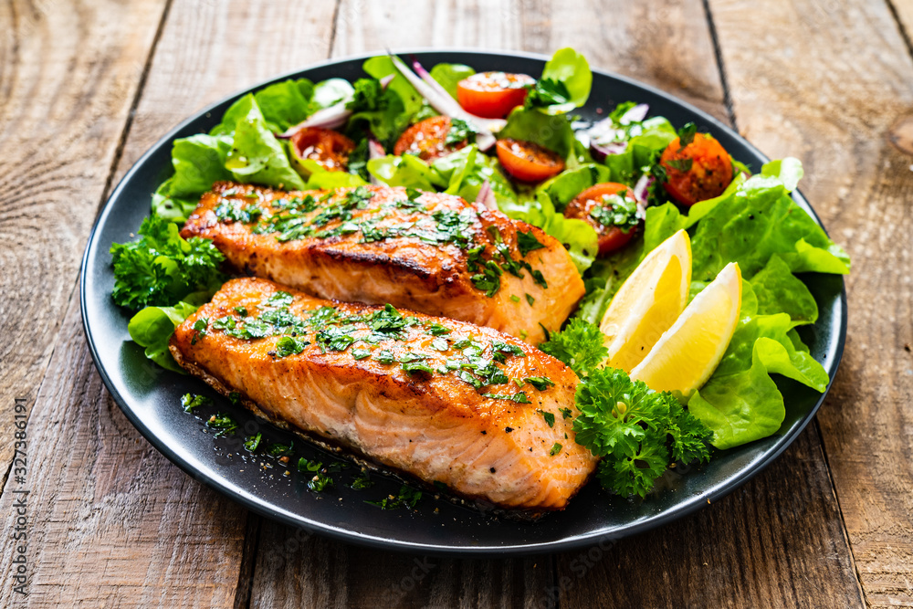 Fried salmon steaks with vegetables on wooden table Fried salmon steaks with vegetables on wooden table