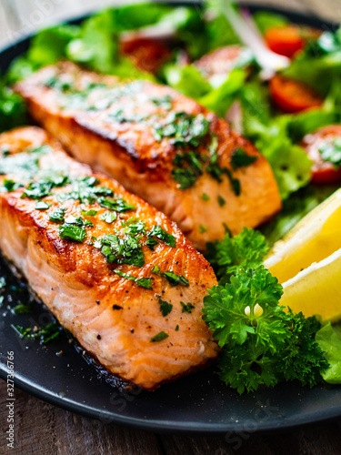 Fried salmon steaks with vegetables on wooden table