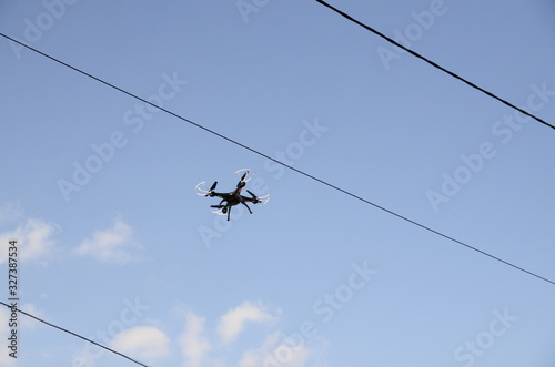 Technology. Against the blue sky, electric wires and a black drone flies.