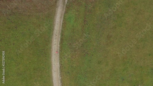 4K aerial drone point of view from directly above flying high over wide grassland leading in to forest with one sporty woman jogging running alone on path  photo