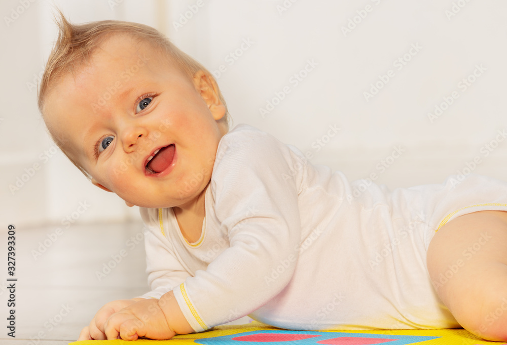 Portrait of laughing happy face of toddler baby boy laying on the floor in nursery room looking at camera Portrait of laughing happy face of toddler baby boy laying on the floor in nursery room looking at camera