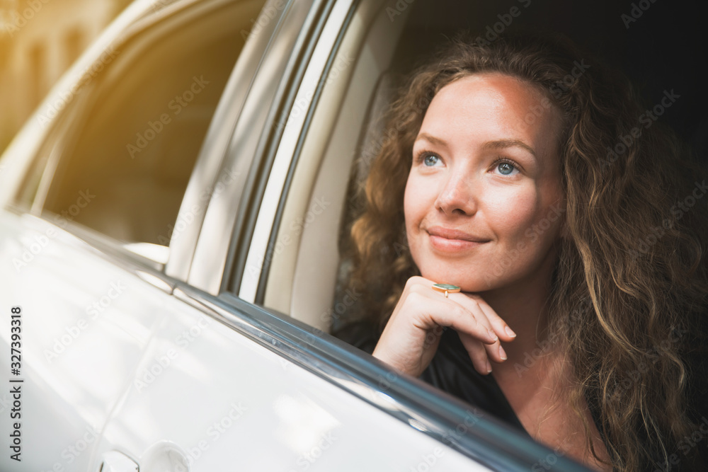 Caucasian beautiful female with a little smile sitting inside the car and looking outside car window. Automobile rental and leasing business. Optimistic friendly woman.