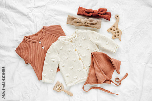 Set of  baby rompers, hat,  hairband and  knitted jumper on white bed. Fashion  baby clothes and accessories. Flat lay, top view