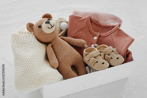 Box with baby stuff and accessories for newborn on bed. Gift box with knitted blanket, clothes, socks, shoes and toy. Baby shower concept.  Flat lay, top view photo