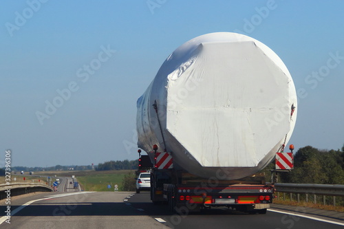 Obraz na płótnie Loaded lowbed semi truck with big barrel tented construction move on asphaly road, rear view, oversized transport logistics w salonie