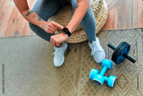 Woman checking her workout time at home. Sport, fitness, lifestyle, technology and people concept - woman setting heart-rate watch.
