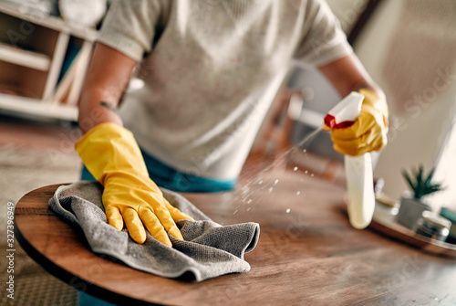 Cropped image of a beautiful young woman makes cleaning the house. Girl rubs dust. Woman in protective gloves is smiling and wiping dust using a spray and a duster while cleaning her house. photo