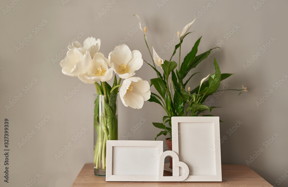 Bouquet of fresh white tulips and empty photo frames with copy space on shelf in front of wall. Mock up with Frame and white Tulips. Mother's Day, Women's Day, March 8, spring greeting card template. Bouquet of fresh white tulips and empty photo frames with copy space on shelf in front of wall. Mock up with Frame and white Tulips. Mother's Day, Women's Day, March 8, spring greeting card template.