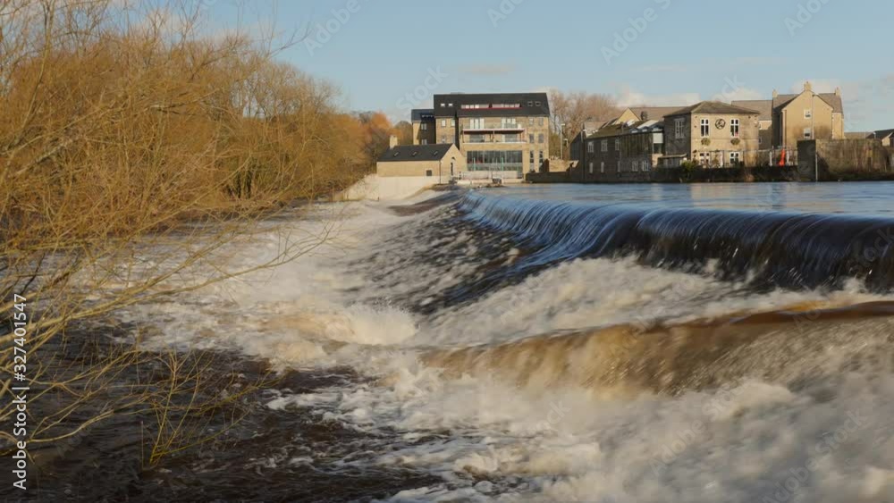 An overflowing river in Yorkshire during the UK floods with a a fast waterfall crashing down stream An overflowing river in Yorkshire during the UK floods with a a fast waterfall crashing down stream