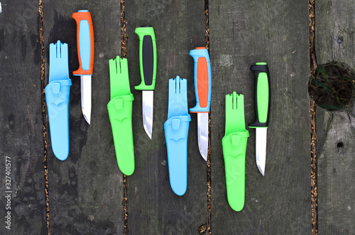 Multi-colored tourist knives on a wooden background.