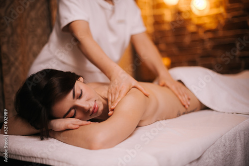 Portrait of young relaxed woman lying on massage table, receiving back and shoulder massage at the spa salon. Concept of luxury professional massage. Concept of body care.