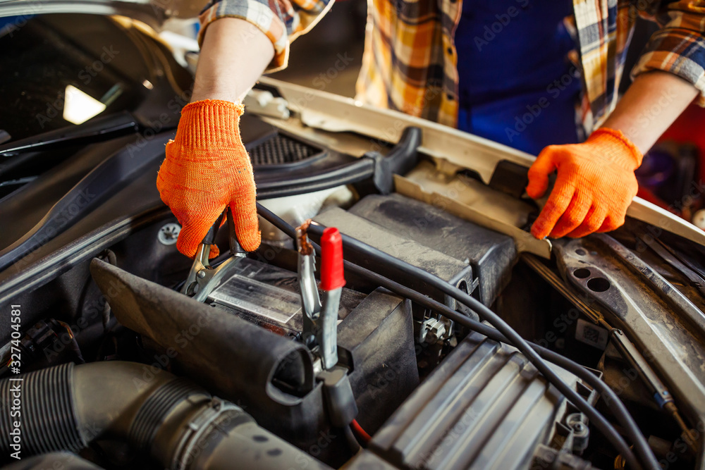 Car mechanic charging the battery using wire cables, cropped shot