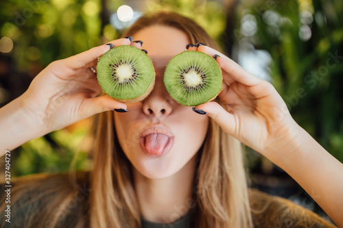 Wallpaper Mural Happy young and blonde woman holding kiwi in front of eyes