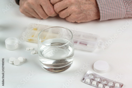 pills and glass of water near elderly man on white table