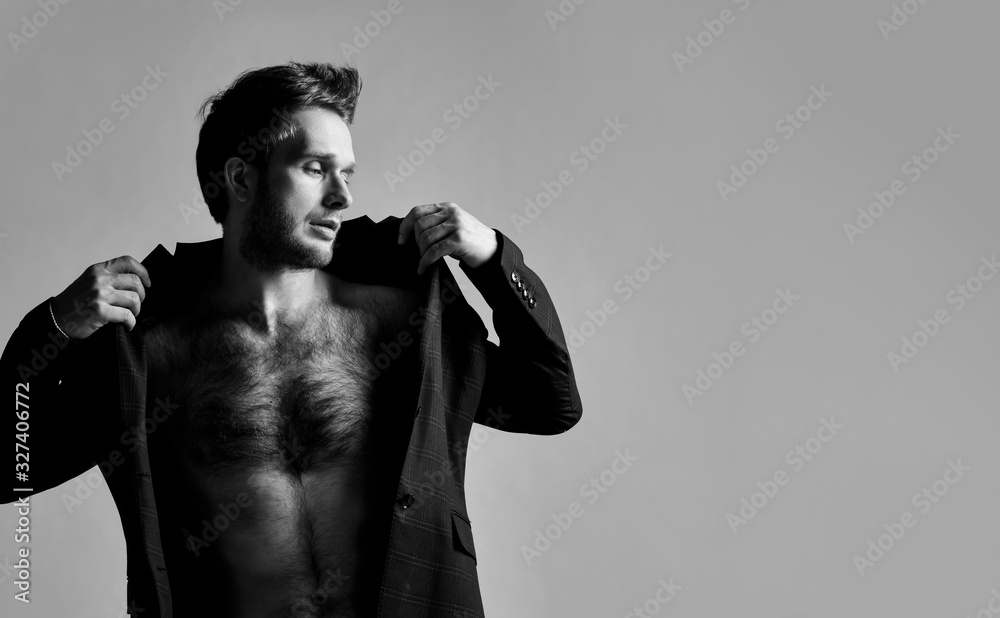 Obraz premium black and white photo of man in black classic suit on naked body. He is straightening his jacket, posing against gray background. Close up