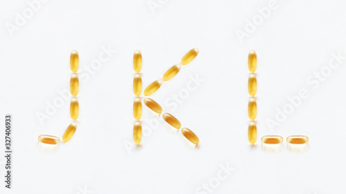 Letters J, K, L made of transparent yellow pills. Part 4 of latin alphabet in medical style. Isolated on white background.