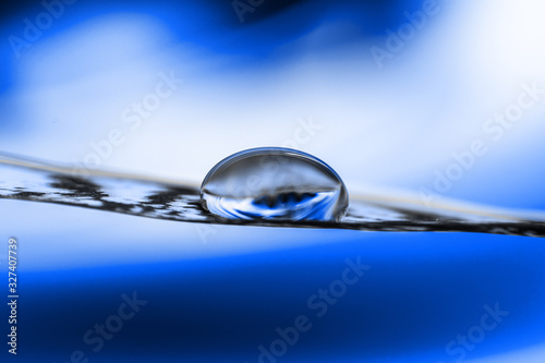 Water drop on a feather close-up on a blue background - Zen concept, dream, purity, tranquility - Focus on the drop, blurred background