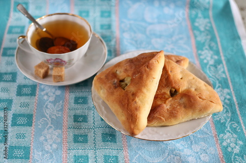 Traditional Tatar dish  echpochmak - a triangle in a plate on a green towel. A cup of traditional Tatar tea with prune and dried apricots. photo