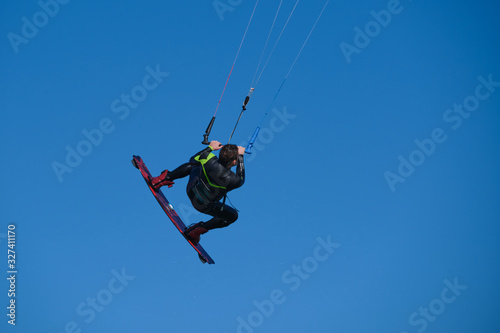 Kitesurfer in wetsuit in the jump on a background of blue sky