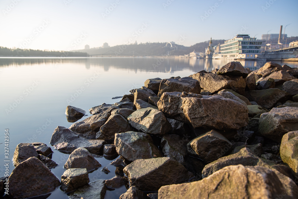 Stones on the river bank. The rays of the rising sun are reflected from the water.
