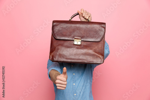 young casual guy hiding behind suitcase and making thumbs up sign