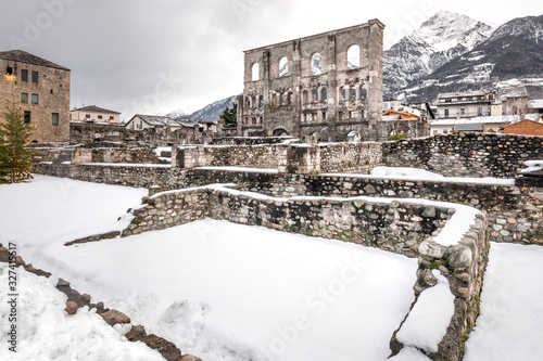 Wide angle view of the snow-covered ruins of the Roman theater of Aosta, under a cloudy sky