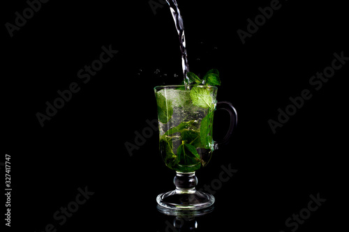 Glass, ice, mint. Glass on a black background. Glass with reflection. Mojito on a black background.