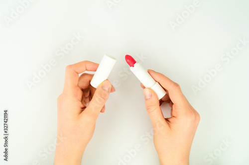 The girl is holding a red lipstick. Tries the product, evaluates.