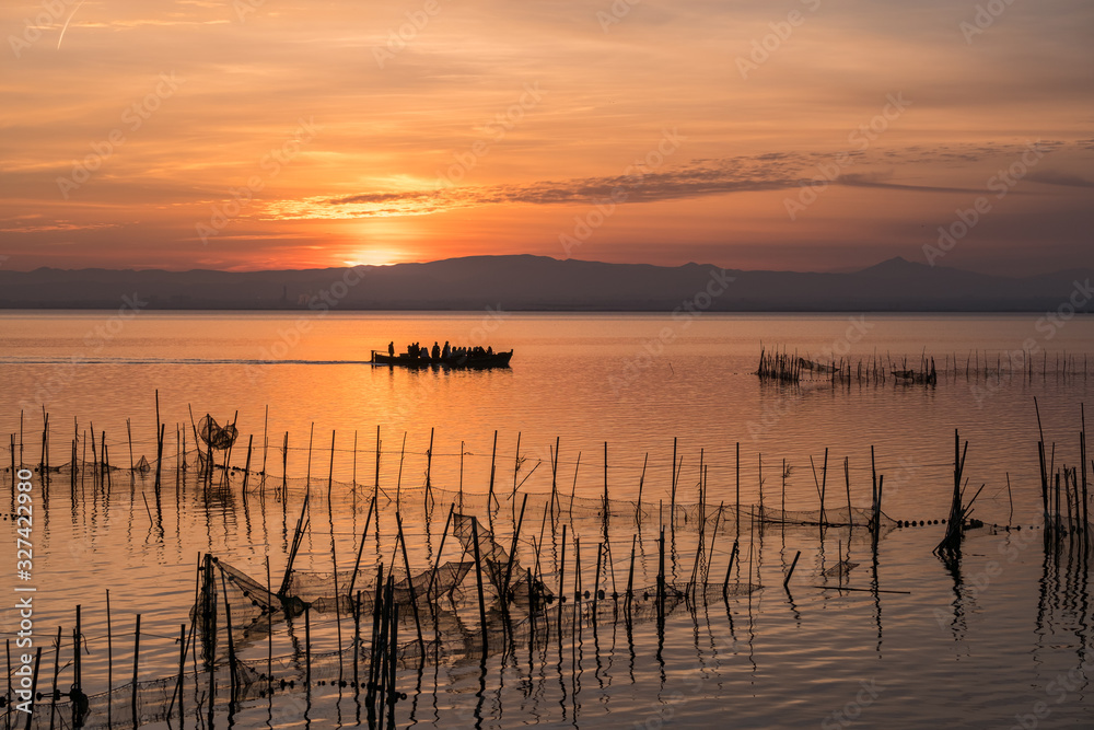 Sunset pier Albufera Valencia tourist ride boat reflections orange sky in the lake Naural Park Spain. traditional fishing nets in the water Sunset pier Albufera Valencia tourist ride boat reflections orange sky in the lake Naural Park Spain. traditional fishing nets in the water